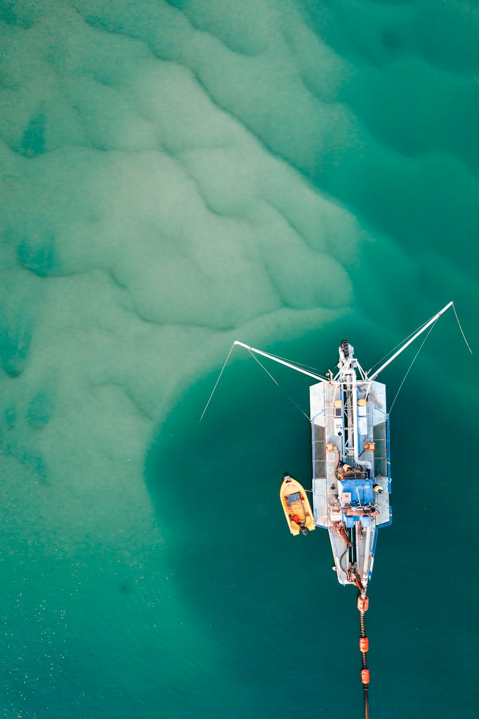 A large dredging vessel floats with a smaller yellow boat nearby.