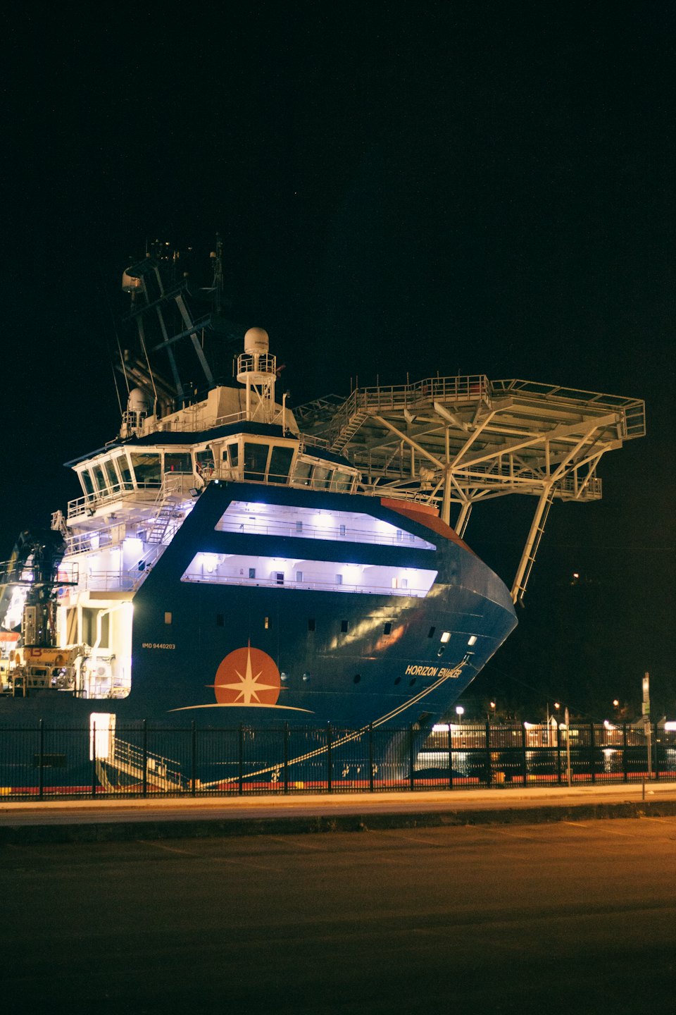 An industrial support vessel docked at a concrete pier at night.